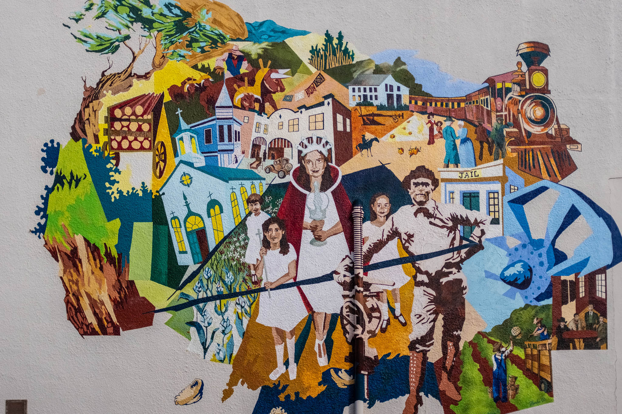 Colorful mural of California history with missions, a train, jail, farm scenes, and people in the foreground