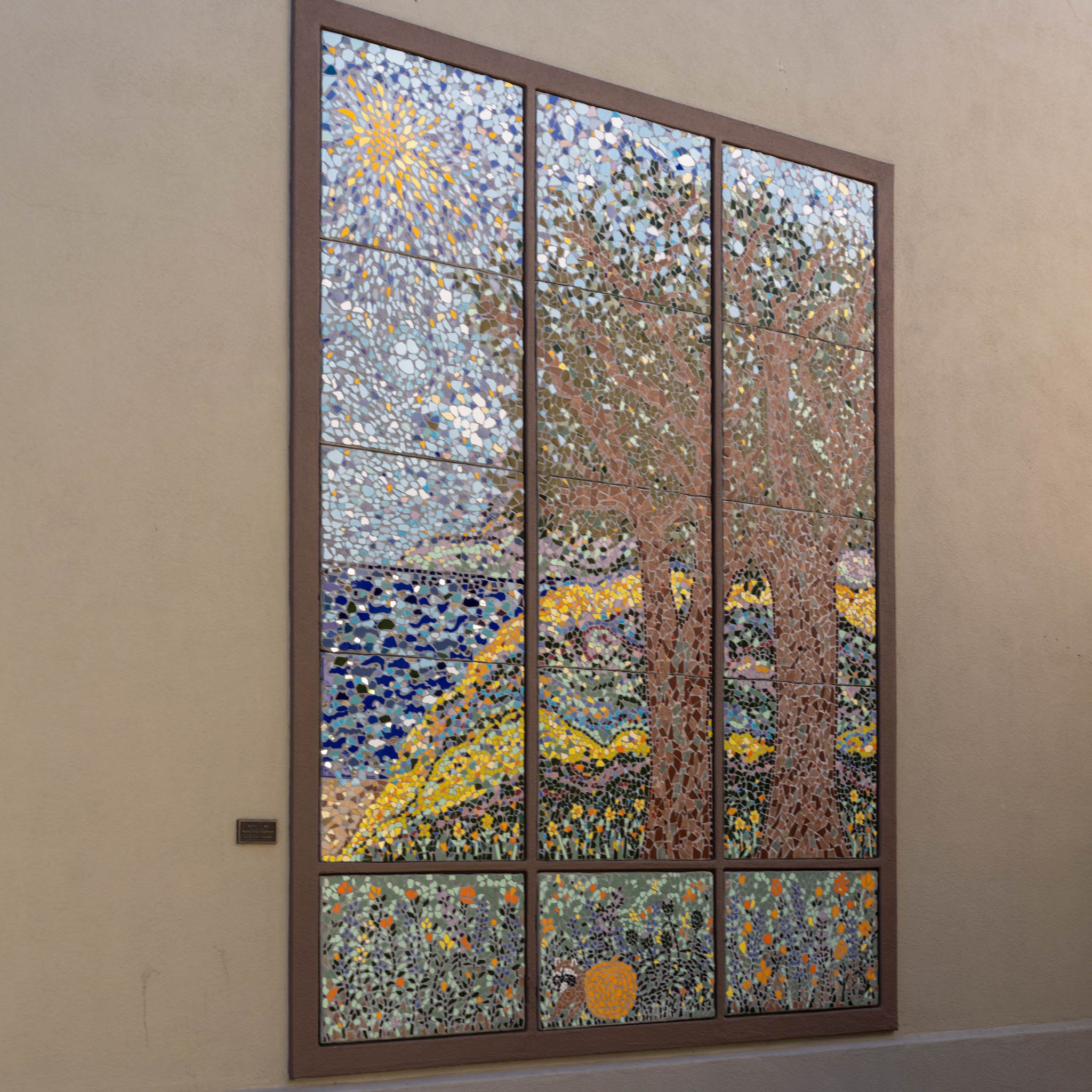 Mosaic wall panel of a landscape with trees, water, flowers, and a bright sunburst in the upper left.