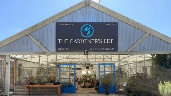 Greenhouse storefront with a sign reading “THE GARDENER’S EDIT” and “GARDENWARES” and “STARTERS” above blue doors