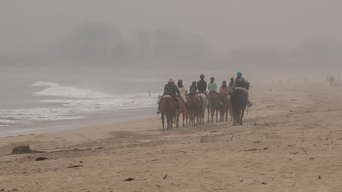 Unrecognizable people riding horses on a smoky day at Poplar Beach near Half Moon Bay, California