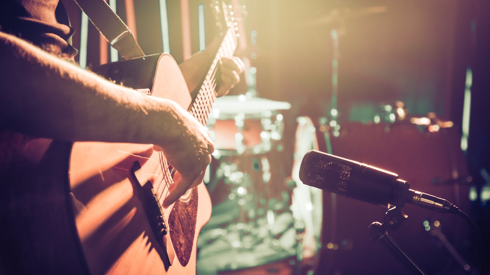 The Studio microphone records an acoustic guitar close-up, in a recording Studio or concert hall, with a drum set on a background in out-of-focus mode. Beautiful blurred background of colored lanterns