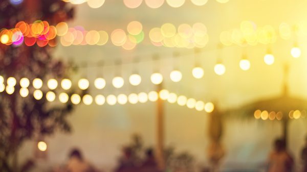 blurred bokeh light on sunset with yellow string lights decor in beach restaurant