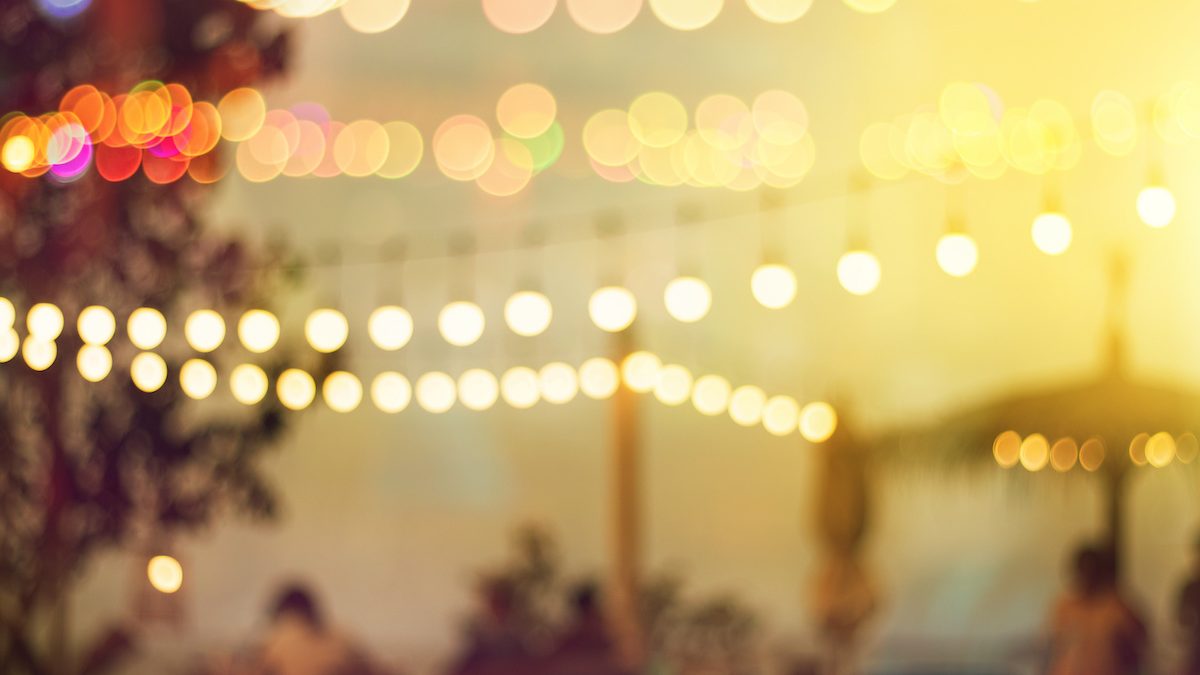 blurred bokeh light on sunset with yellow string lights decor in beach restaurant