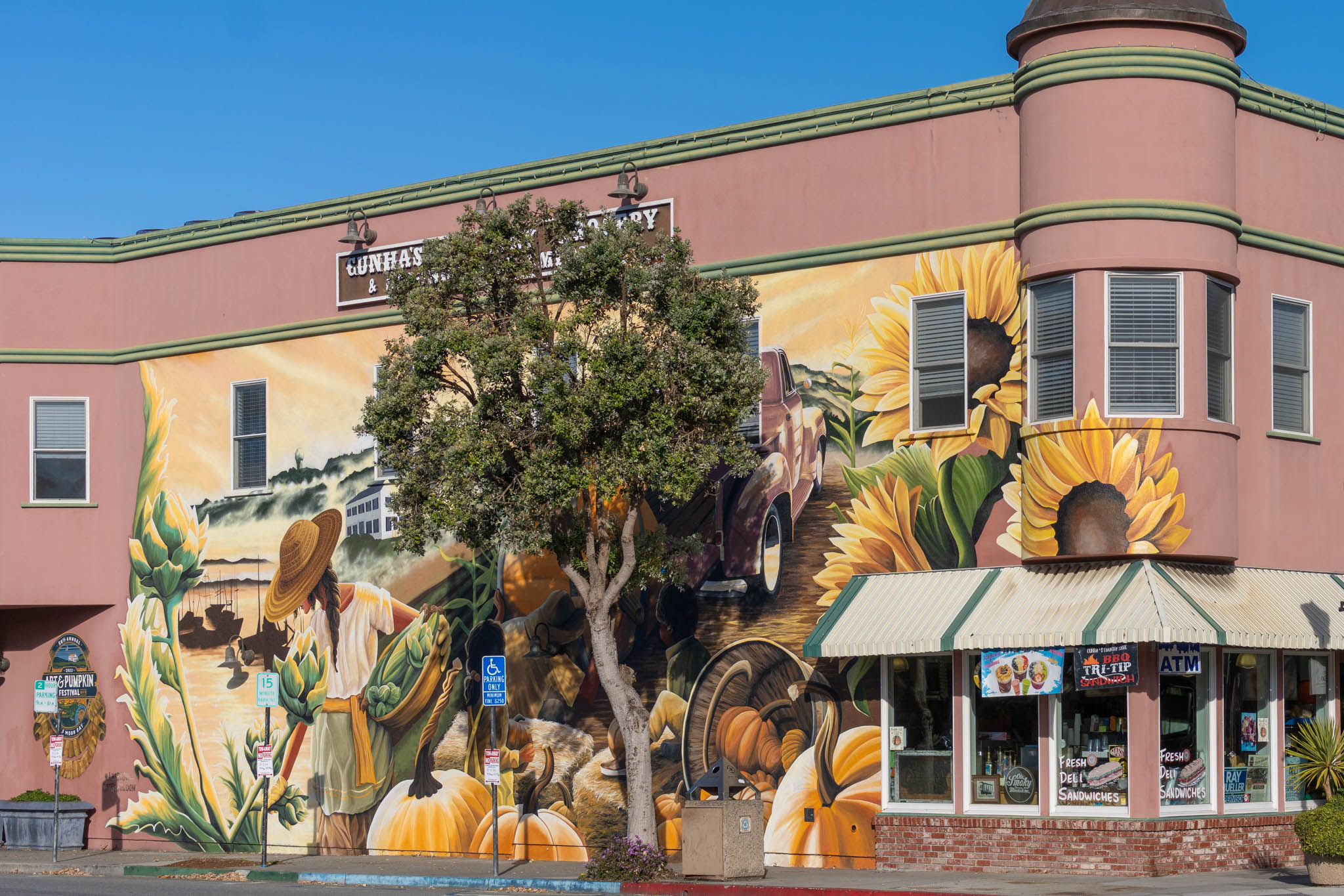 Building with a large mural of sunflowers, pumpkins, and a person in a hat, plus storefront signs and an ATM